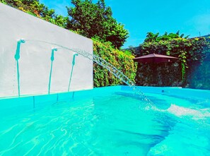 A swimming pool with clear water, a white wall with three water jets, and lush greenery in the background. - ¡casa Maya en Mérida Centro con Alberca! (Mérida)