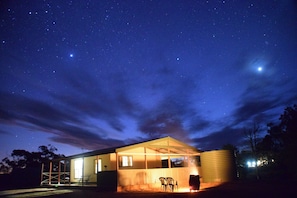 A modern house with a covered porch, a large water tank, and a clear night sky with stars.
