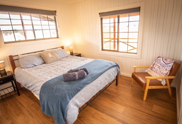 A bedroom with a bed, two bedside tables, a chair, and two windows.