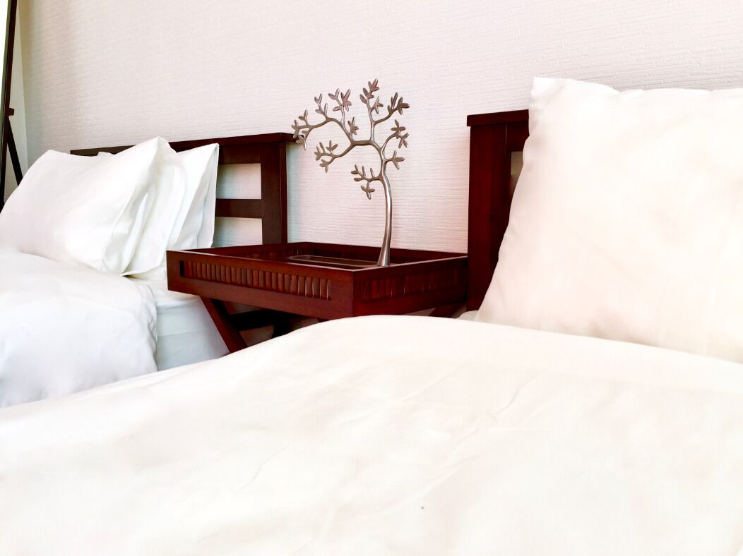 A neatly made bed with white linens and a wooden headboard. A small metal tree decoration is placed on the headboard.
