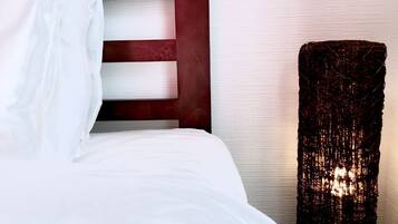 A neatly made bed with white linens and a wooden headboard. A tall, textured lamp stands beside the bed.