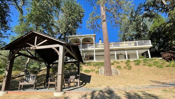 A wooden pavilion with benches, a large building with a balcony, and a clear blue sky. - Creekside Dream - Dog Friendly/Game Room/Sleeps 12 (Oakhurst)