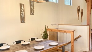 Un'area pranzo con un tavolo in legno apparecchiato per sei persone, un lampadario e una scala con ringhiera in legno.