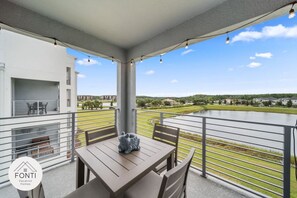 Ein Balkon mit Tisch und Stühlen, der auf ein Gewässer und viel Grün blickt.