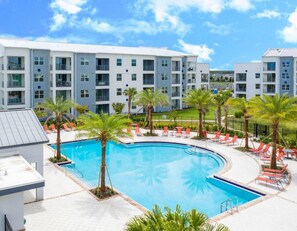 A modern hotel with a swimming pool surrounded by palm trees and sun loungers.