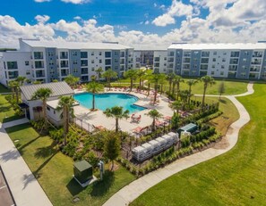 A modern hotel with a central swimming pool surrounded by palm trees and lounge chairs.