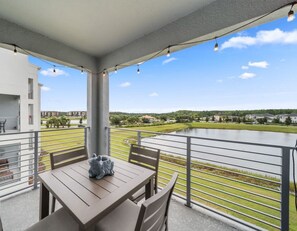A balcony with a table and chairs, overlooking a body of water and greenery.