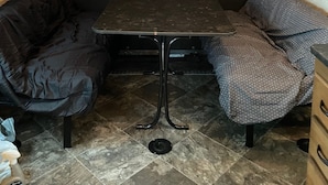 A compact RV interior with a central table, two cushioned seating areas, and a tiled floor. - 19FT RAPTOR RV (Wasilla)