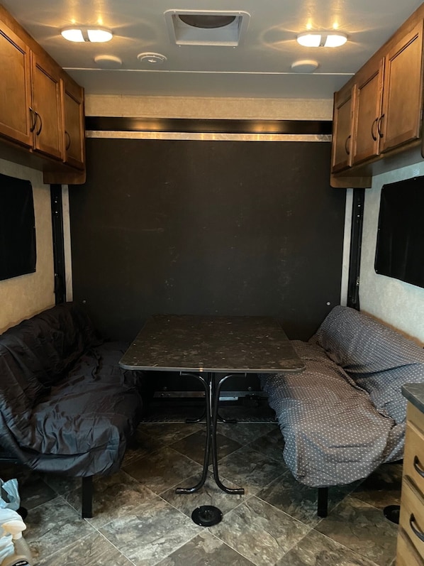 Ein kompaktes Wohnmobil-Interieur mit einem zentralen Tisch, zwei gepolsterten Sitzbereichen und einem gefliesten Boden.