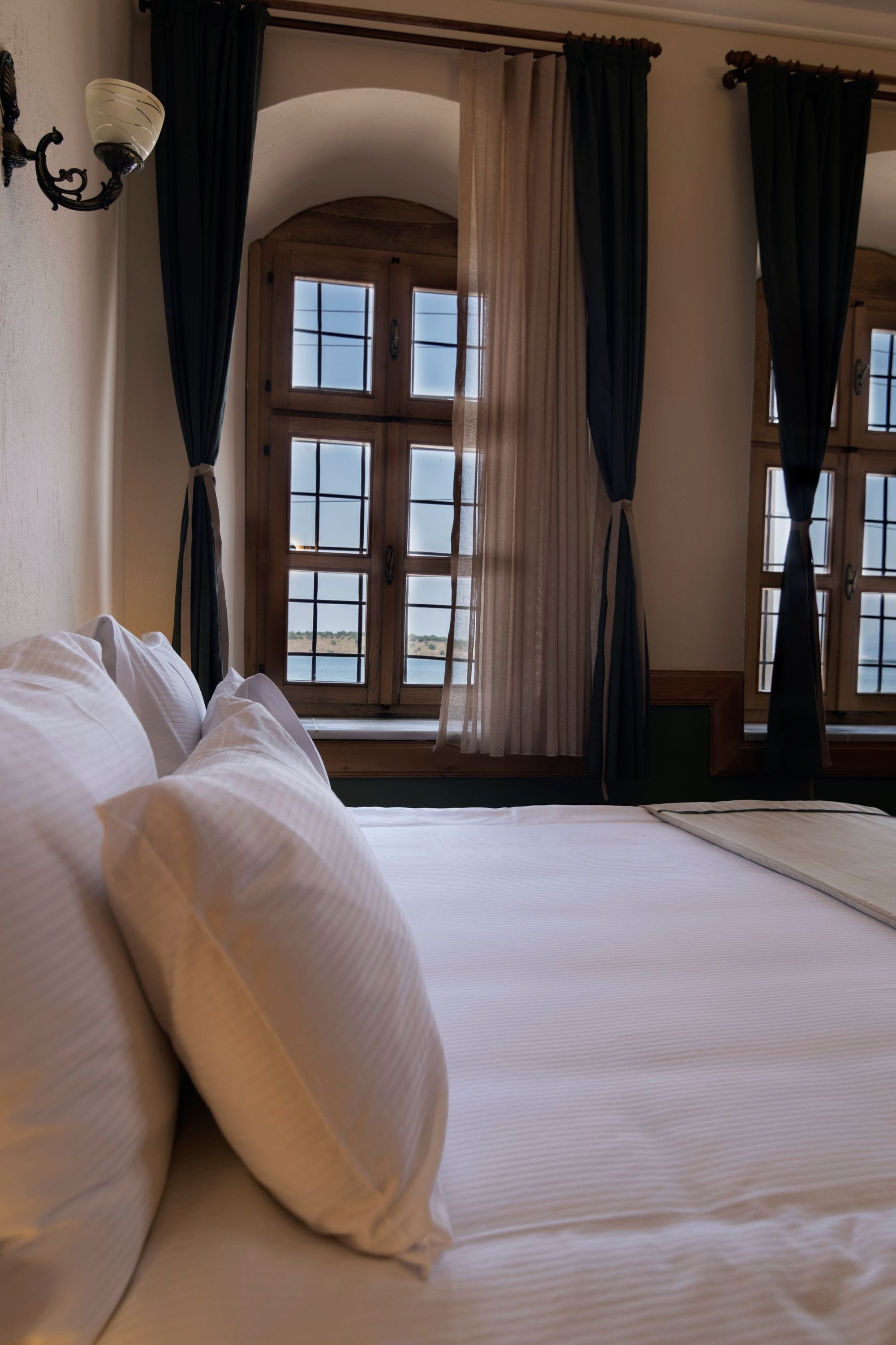 Un dormitorio con una cama grande, una ventana con cortinas y una lámpara de pared.