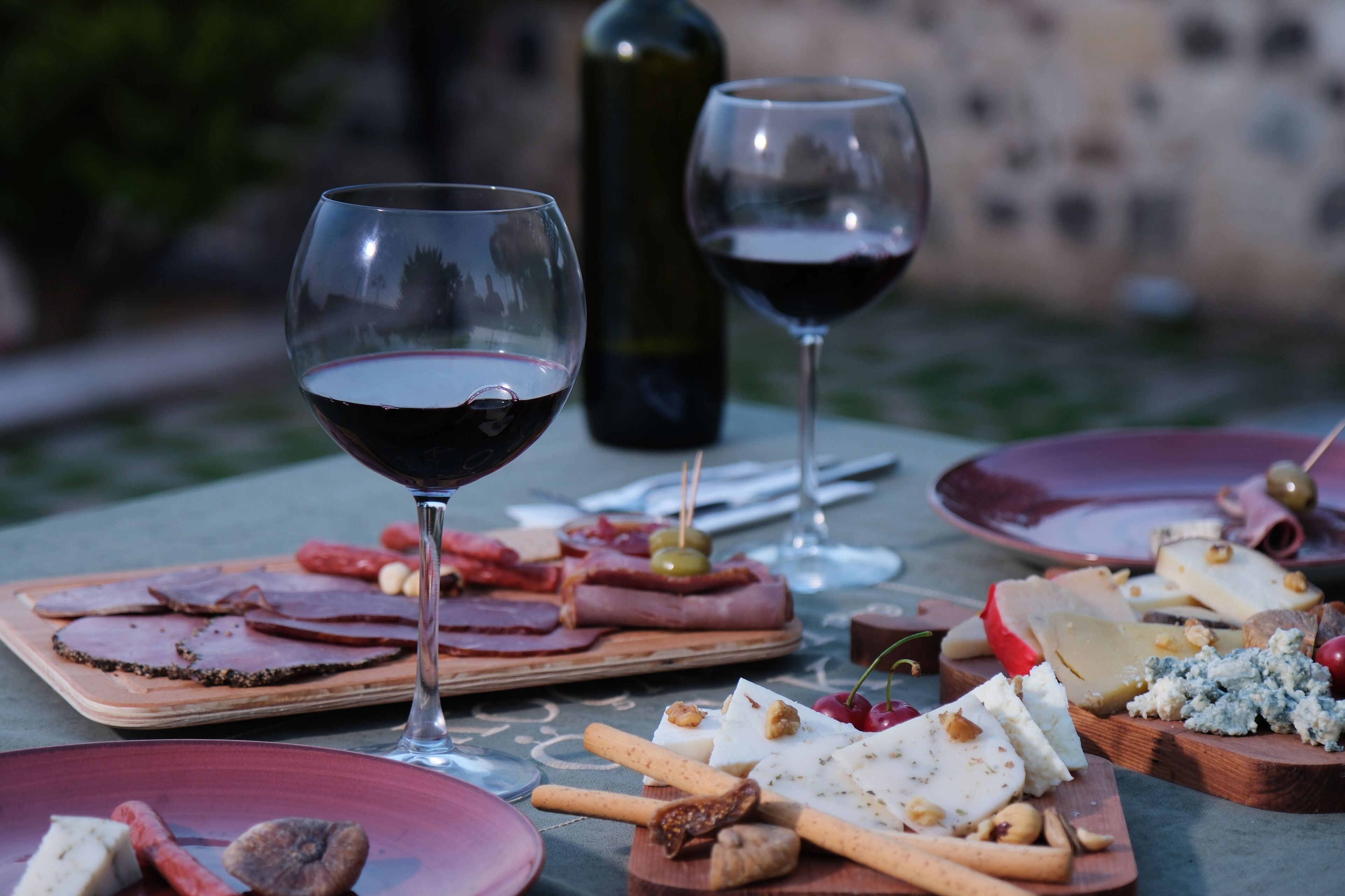 A table set with various cheeses, meats, and crackers, accompanied by two glasses of red wine.