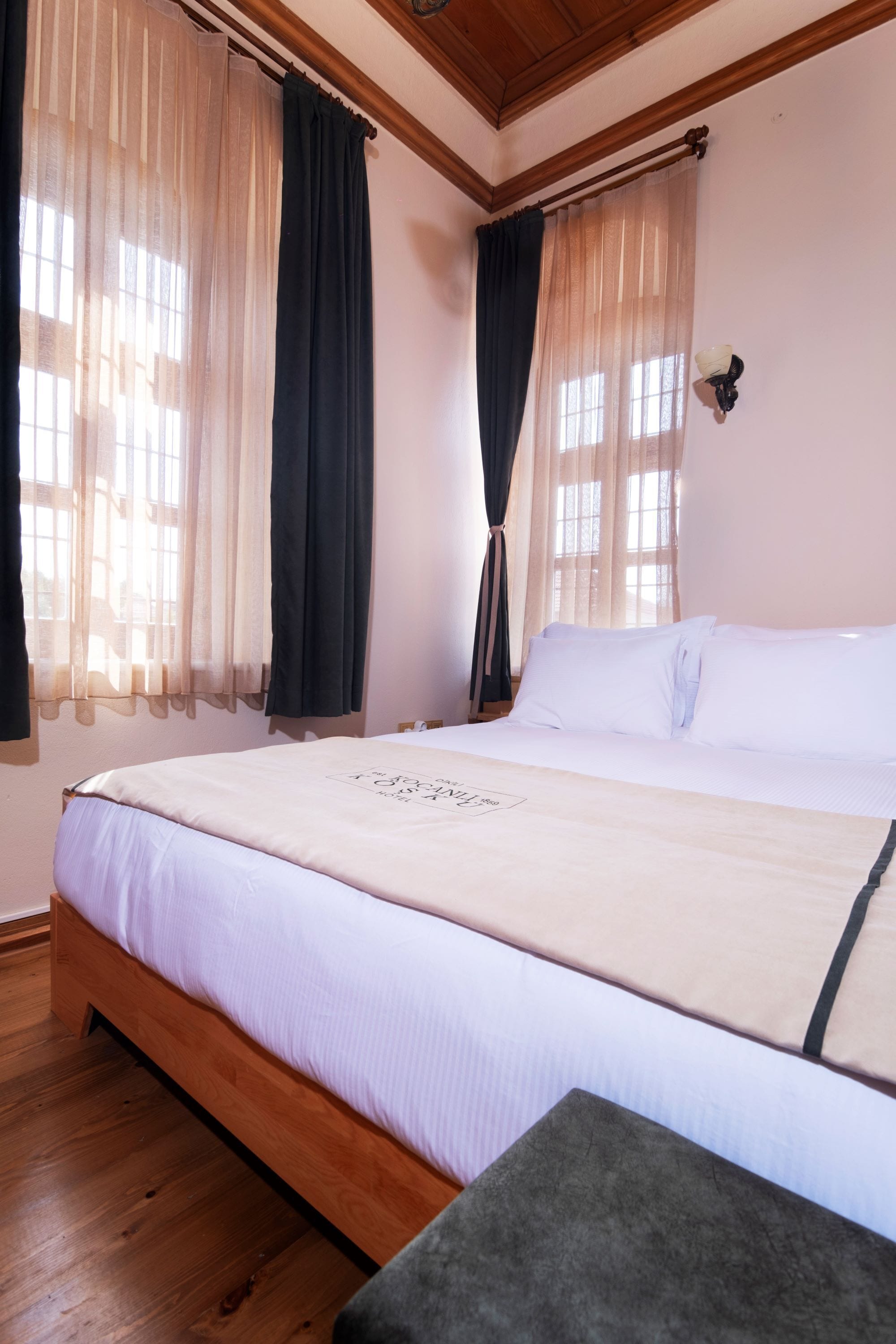 Una camera da letto con struttura letto in legno, biancheria da letto bianca e tende leggere.