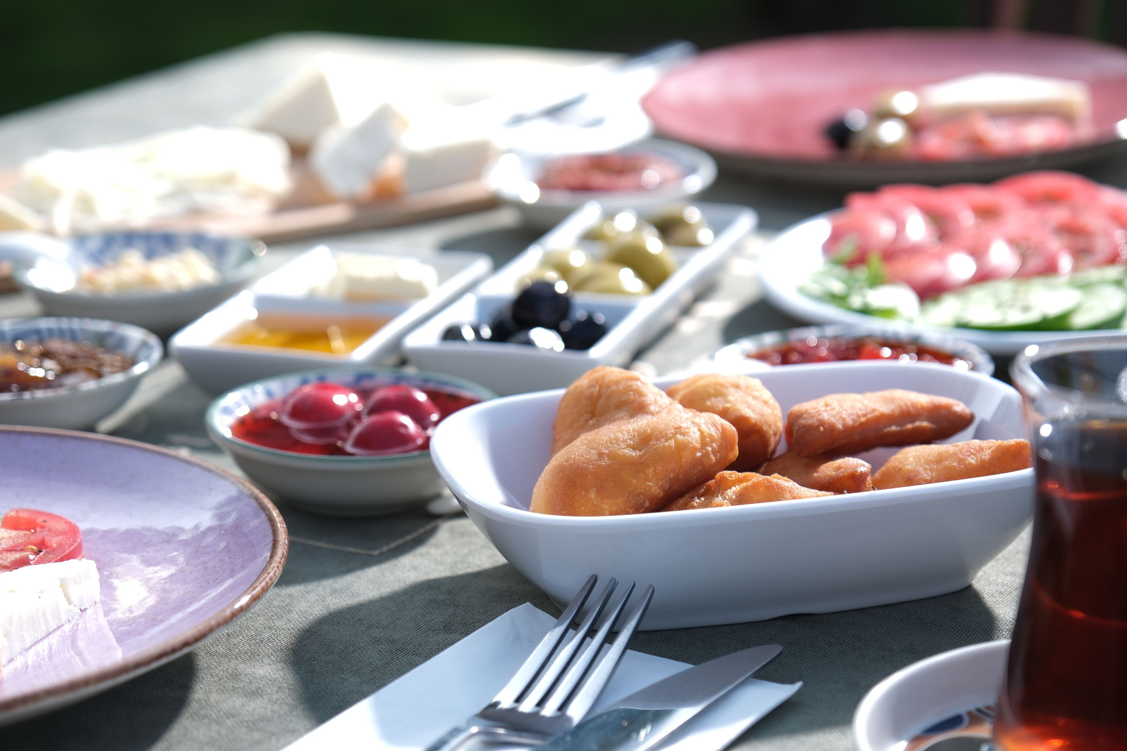 A table with various food items including a bowl of pastries, a plate of sliced tomatoes, and several bowls of different foods.