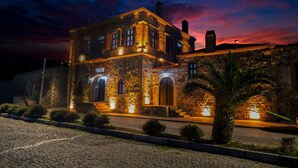Un edificio histórico con muros de piedra y ventanas de arco, iluminado por luces cálidas al anochecer.