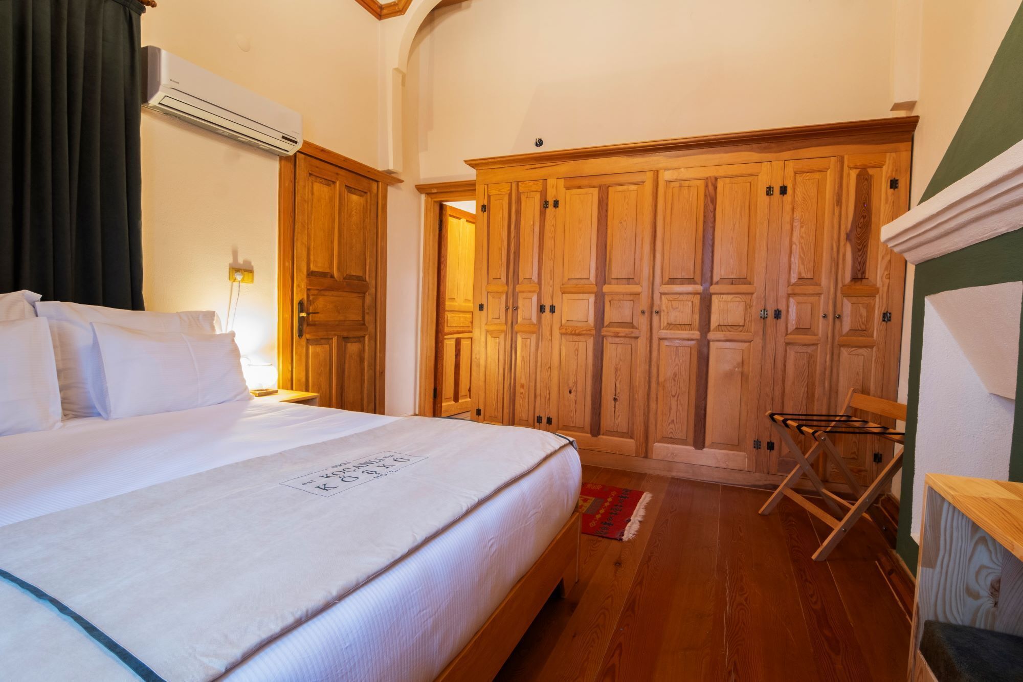 A bedroom with a bed, wooden wardrobe, and an air conditioning unit.