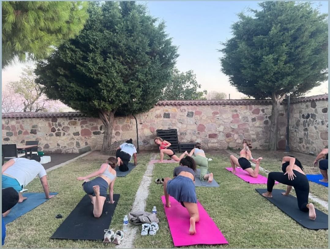 Een groep mensen beoefent yoga op matten, buiten, met stenen muren en bomen.
