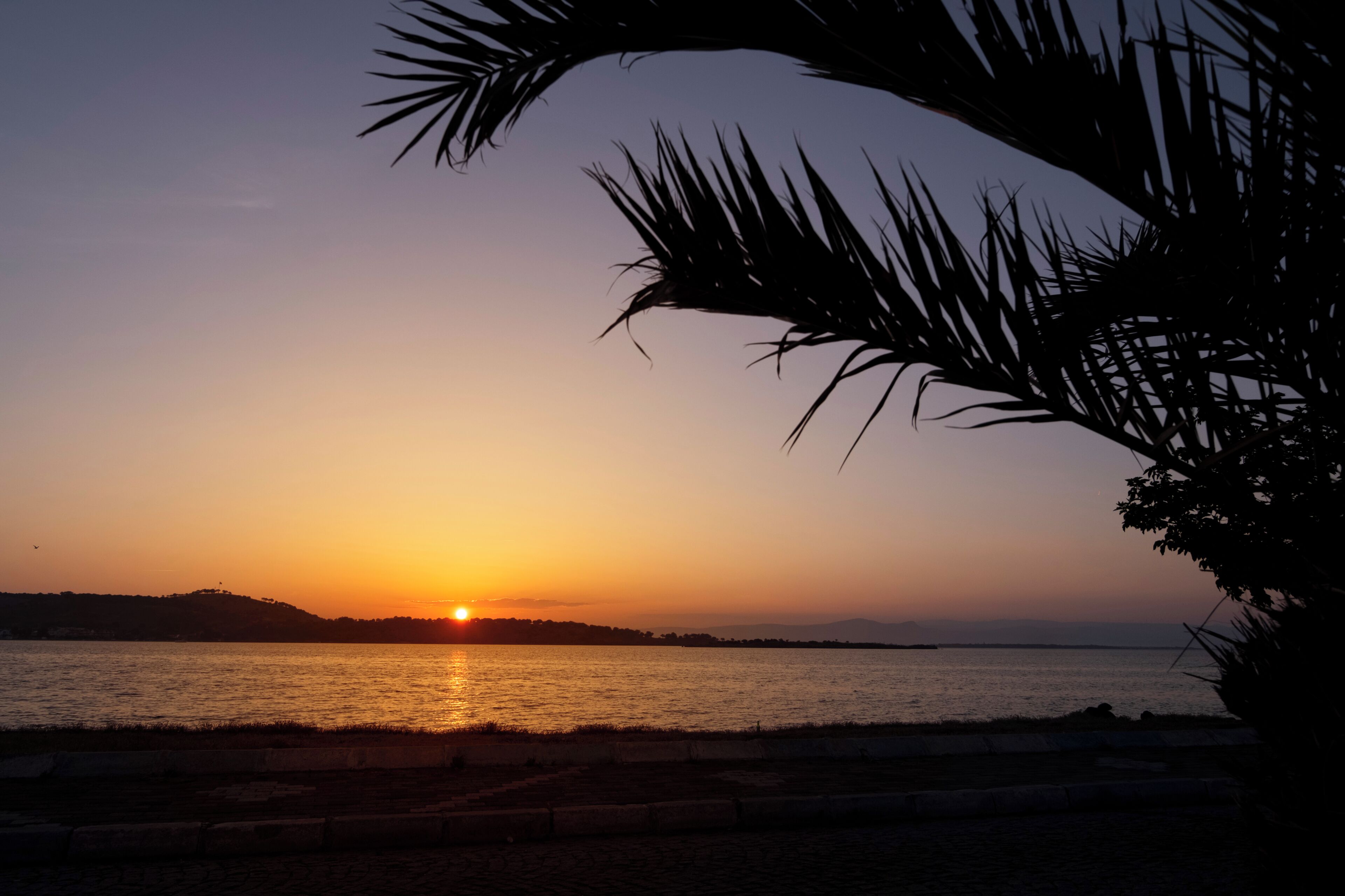 A sunset over a body of water with a silhouette of a landmass in the distance.