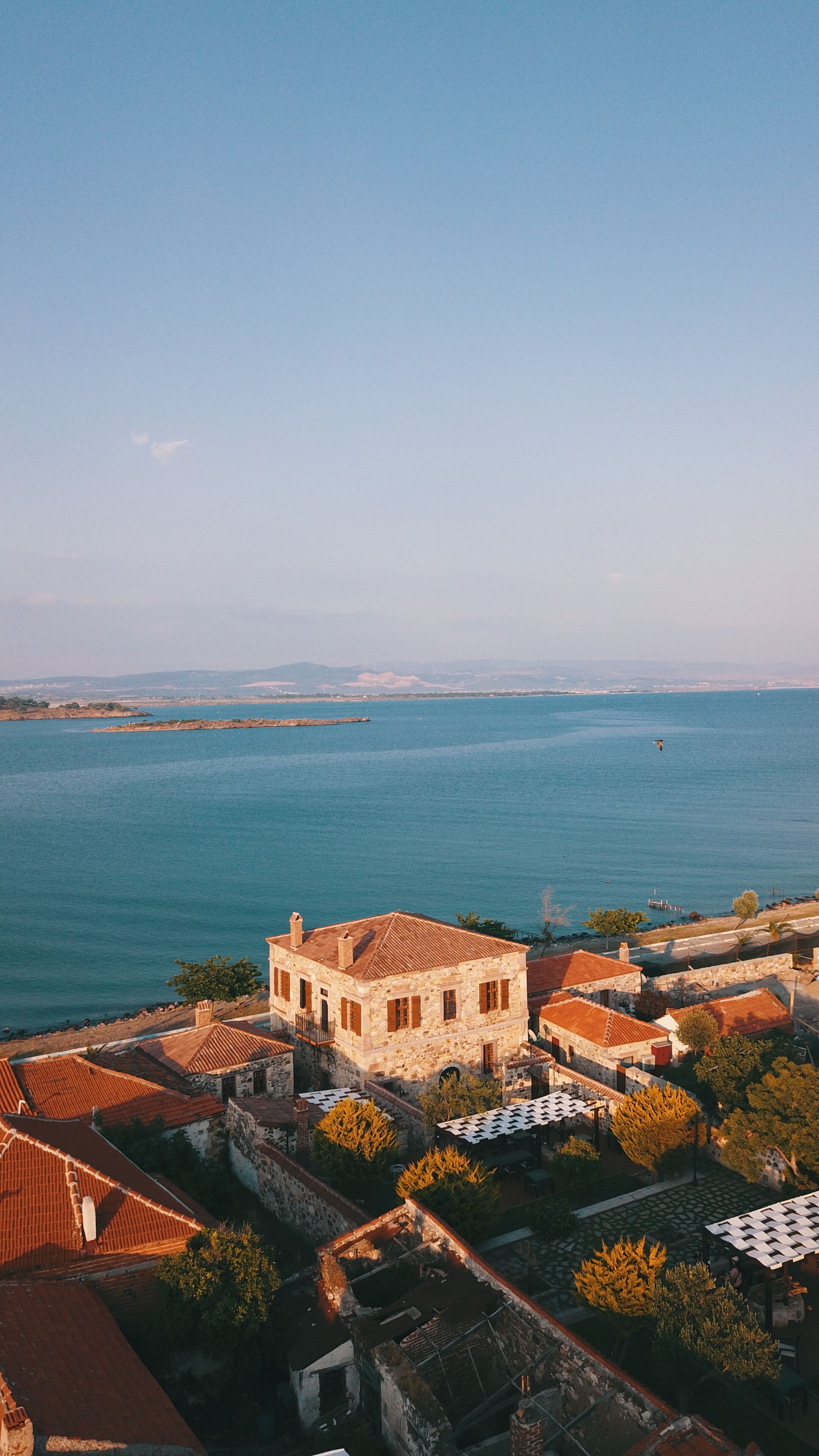 A coastal town with stone buildings, a clear view of the sea, and a distant city skyline.