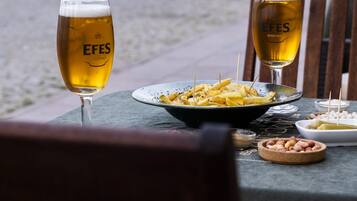 A table with two glasses of beer, a plate of food, and a wooden chair.