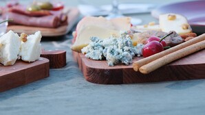 Una tabla de quesos con varios tipos de queso, una copa de vino tinto y cubiertos de madera sobre una mesa.