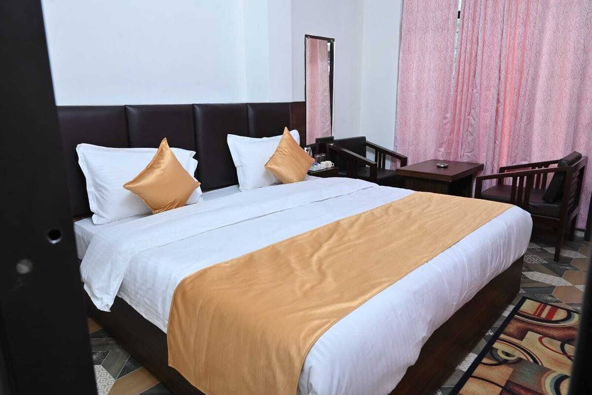 Quarto de hotel com cama, mesa de cabeceira, cadeira e espelho.