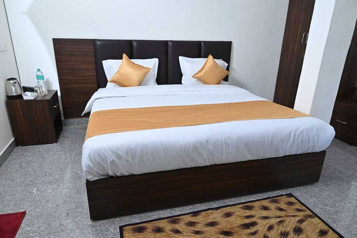 Quarto de hotel com uma cama grande, cabeceira escura, roupa de cama branca e piso de madeira.