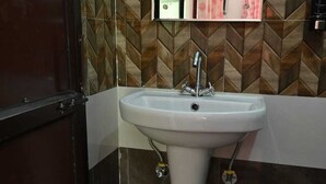 A bathroom with a white pedestal sink, a mirror above it, and a herringbone-patterned tile backsplash. - Akansha The Lake View (Nainital)