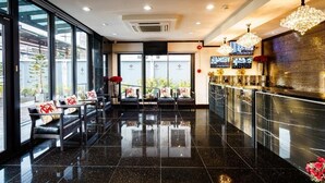 A modern hotel lobby with a bar area, seating with red cushions, and large windows. - Lux Boutique Hotel (Nonthaburi)