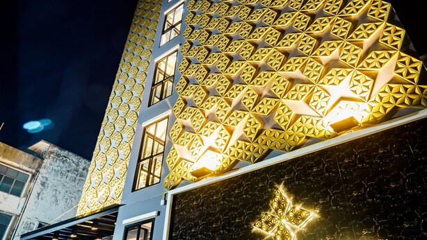 A hotel with a distinctive facade featuring a geometric pattern and illuminated signage. - Lux Boutique Hotel (Nonthaburi)