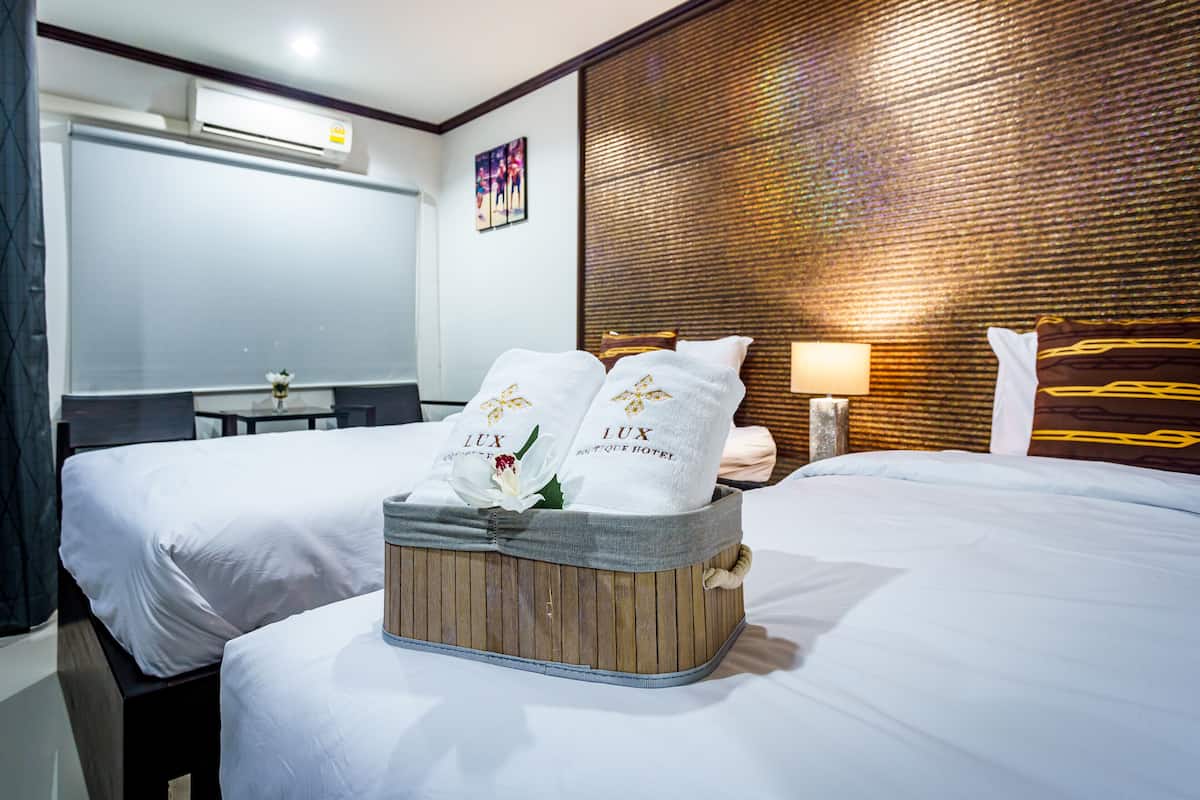 Ein Hotelzimmer mit zwei Betten, einem Holzkopfteil, einem kleinen Tisch und einer Wandklimaanlage.