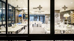 A Lux Boutique Hotel dining area with white furniture and a central floral arrangement. - Lux Boutique Hotel (Nonthaburi)