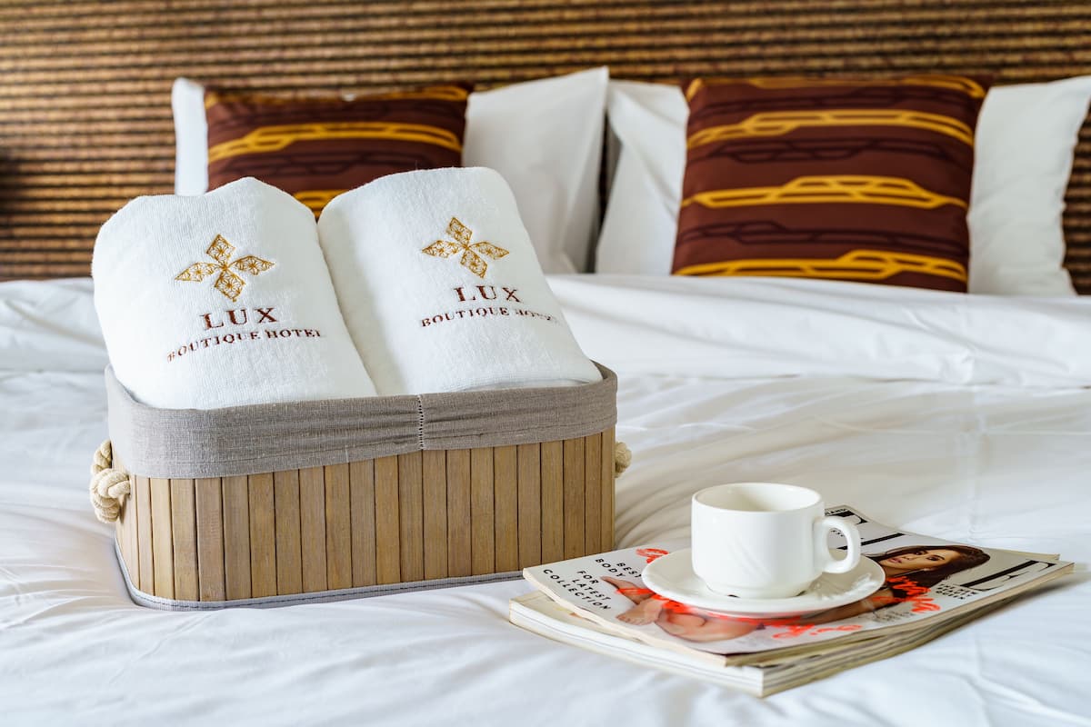 Ein Bett mit weißer Bettwäsche, einem hölzernen Kopfteil und einem weißen Kissen mit der Aufschrift 'LUX BOUTIQUE HOTEL'.
