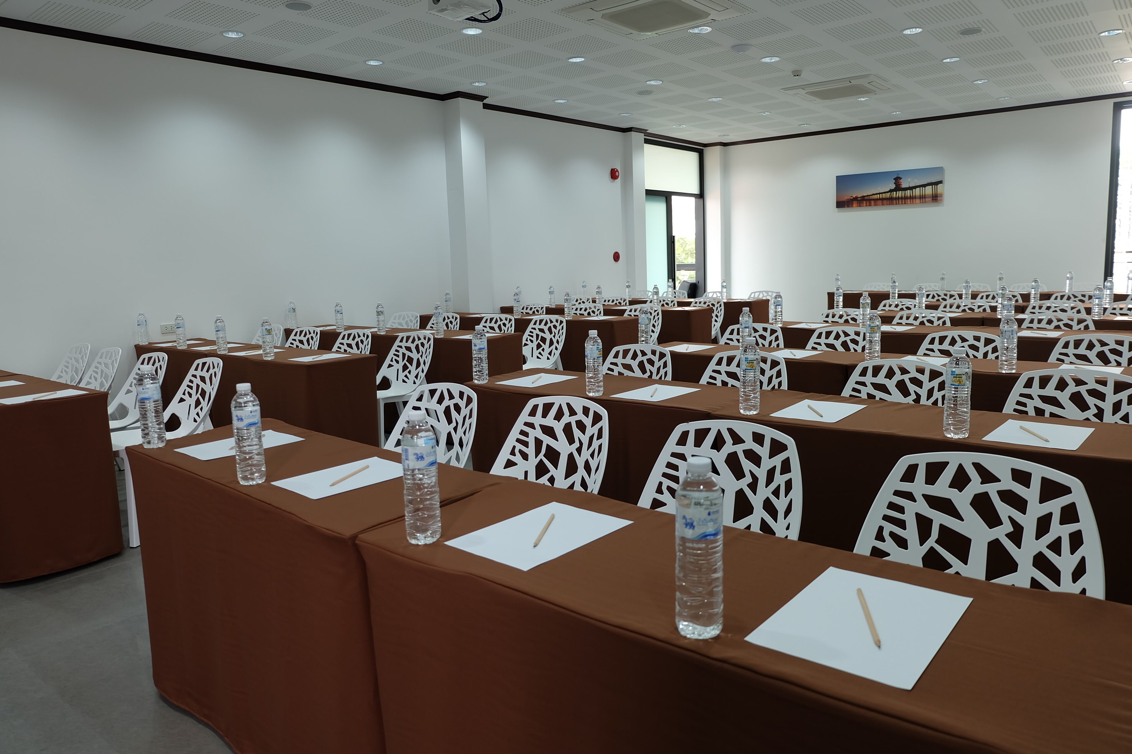 A conference room with rows of brown tables, white chairs, and water bottles.