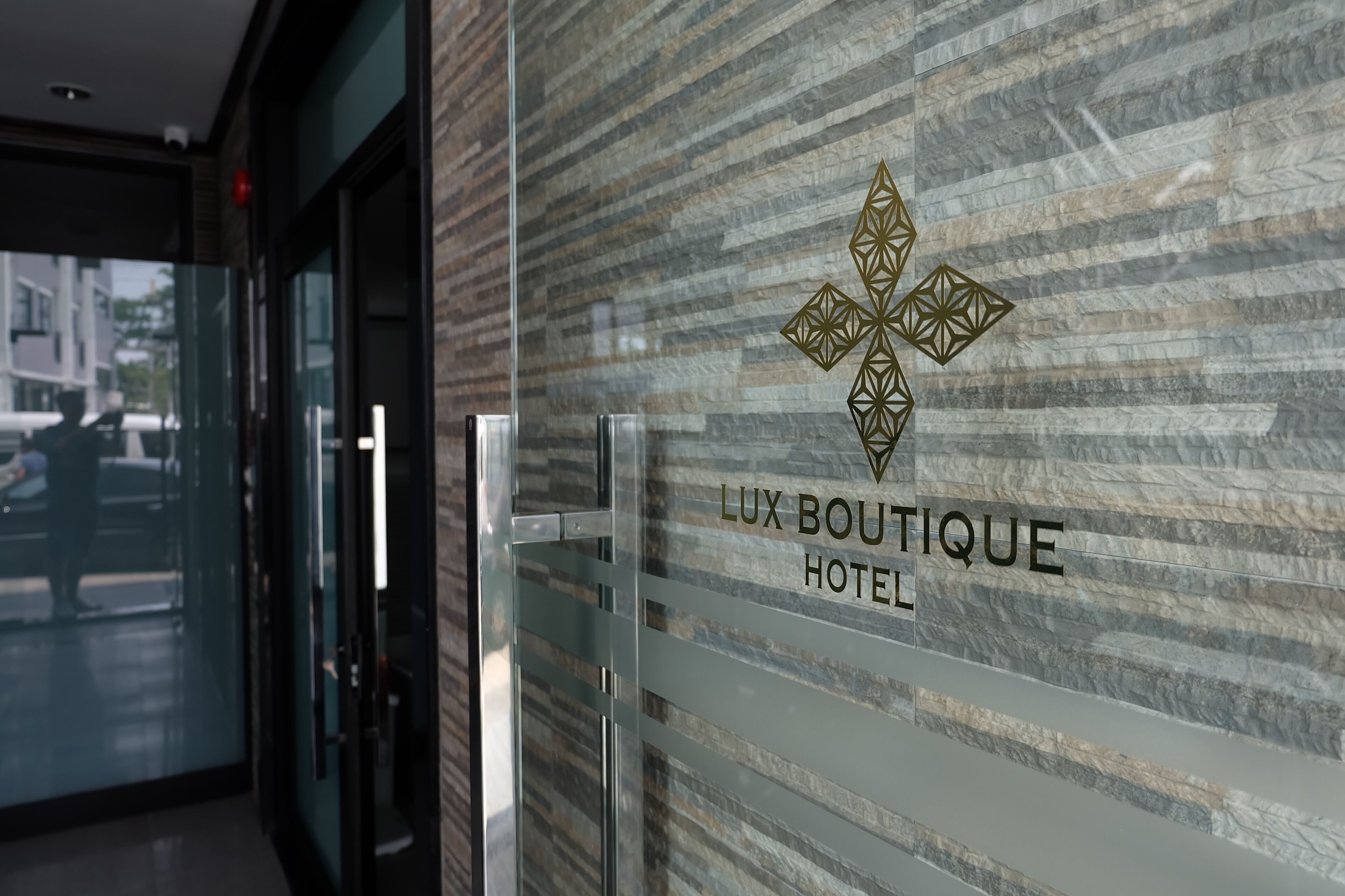 A glass door with a metal handle and a sign that reads "LUX BOUTIQUE HOTEL" with a geometric logo.