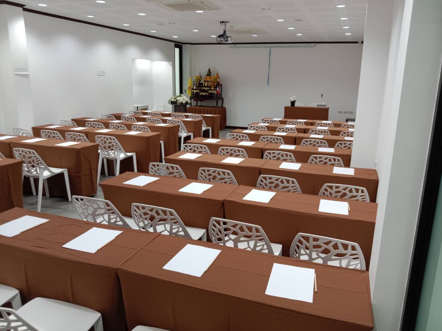 A conference room with rows of tables and chairs, a podium, and a projector screen.