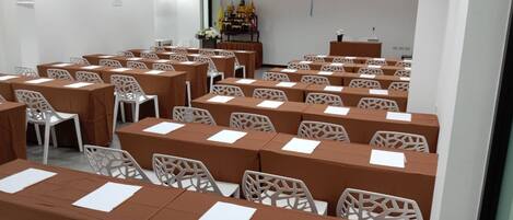 A conference room with rows of tables and chairs, a podium, and a projector screen.
