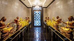 A hallway with a reflective floor, a chandelier, and statues of figures on either side. - Lux Boutique Hotel (Nonthaburi)