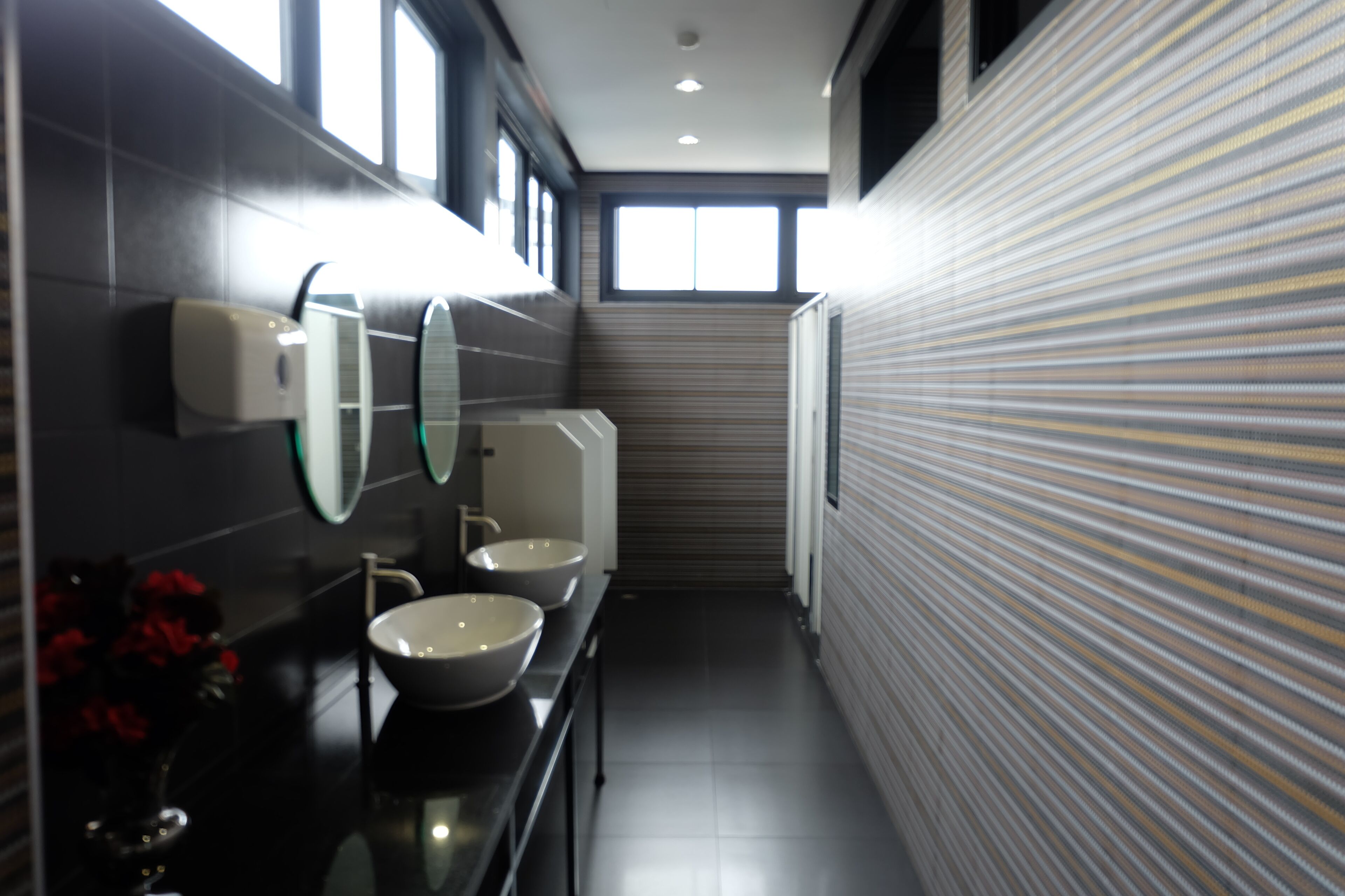 A modern bathroom with a black countertop, two sinks, a mirror, and a toilet.