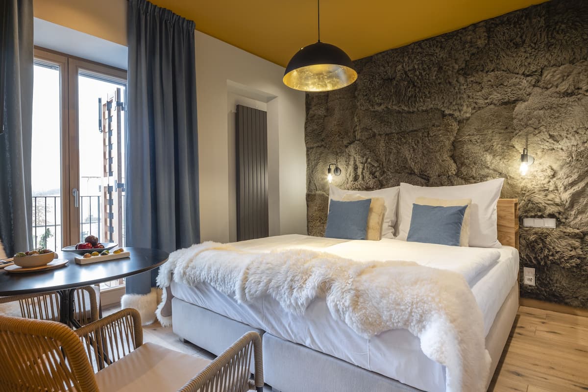 Un dormitorio con una cama grande, una mesa de comedor con sillas, vistas al exterior y una pared de piedra.