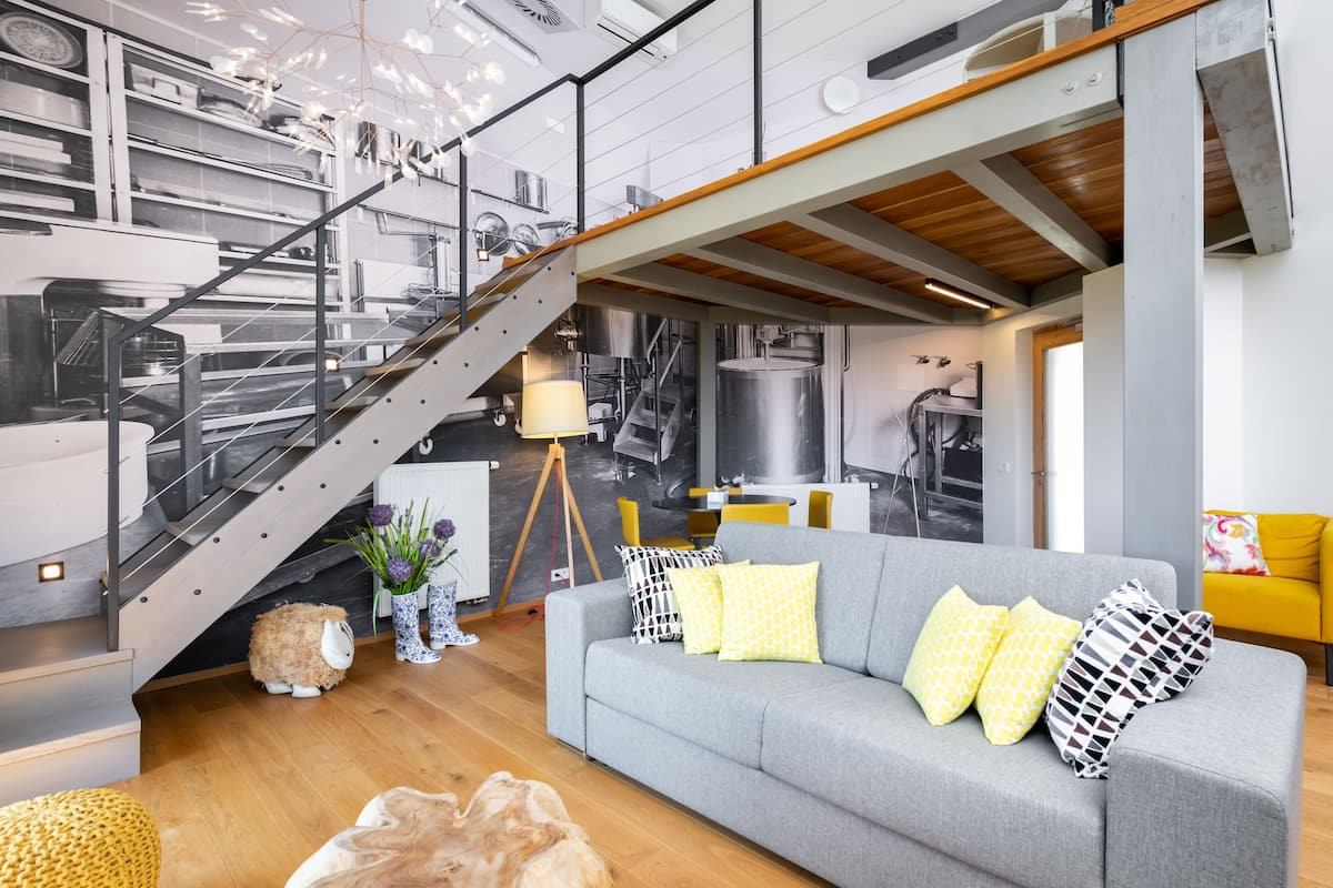 Un interior moderno con una escalera, un sofá gris con cojines estampados y un sillón amarillo.