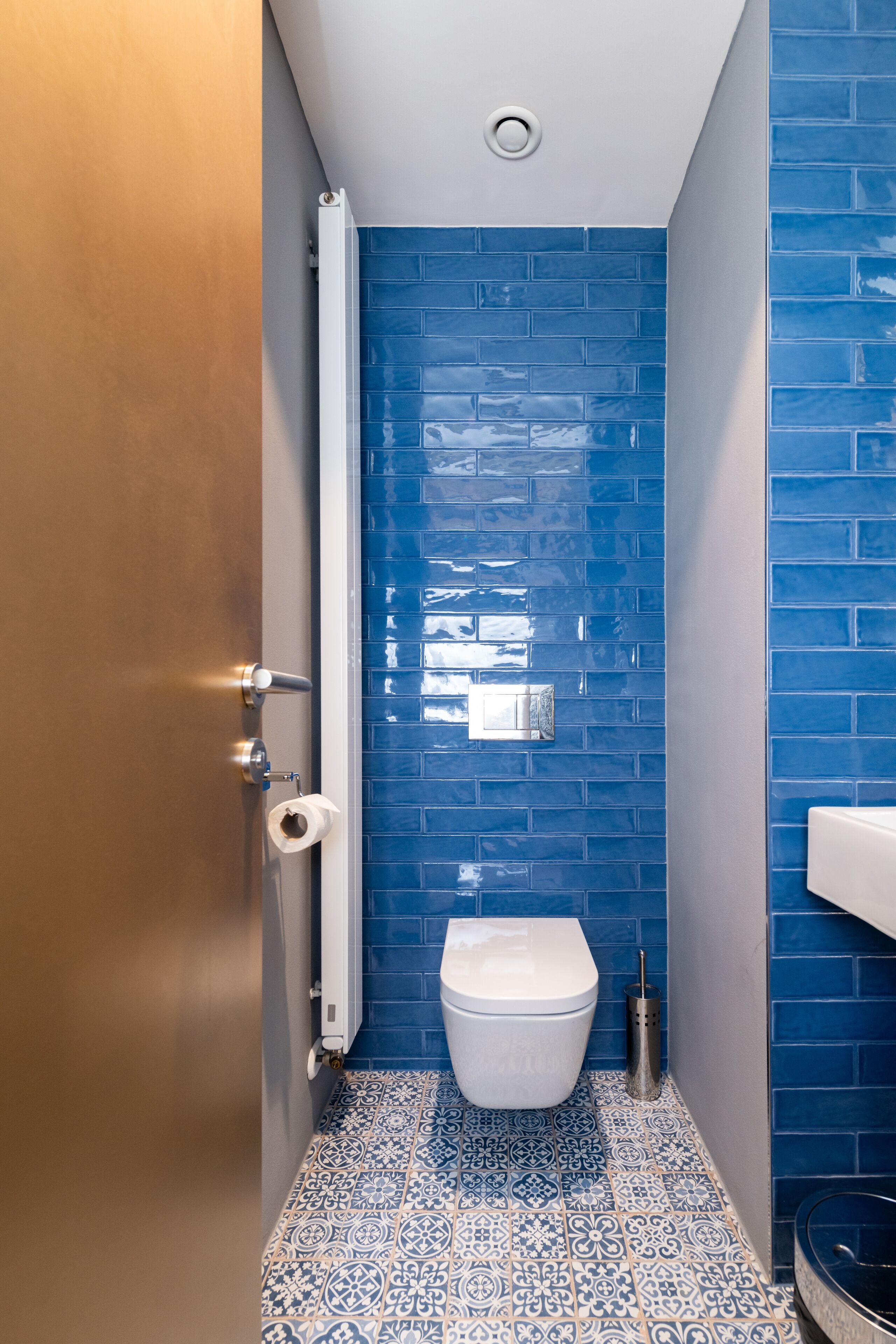 Een badkamer met blauwe betegelde wanden, een wit toilet, vloertegels met een patroon en een handdoekrek.