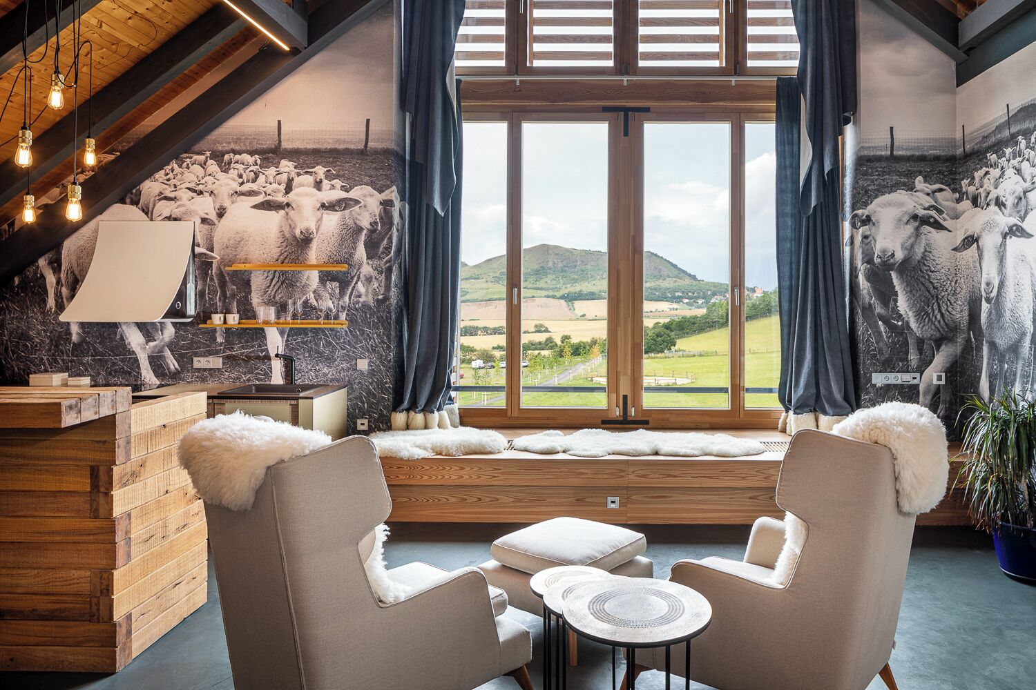 A cozy room with a large window, a mural of sheep, wooden furniture, and a rustic ceiling.