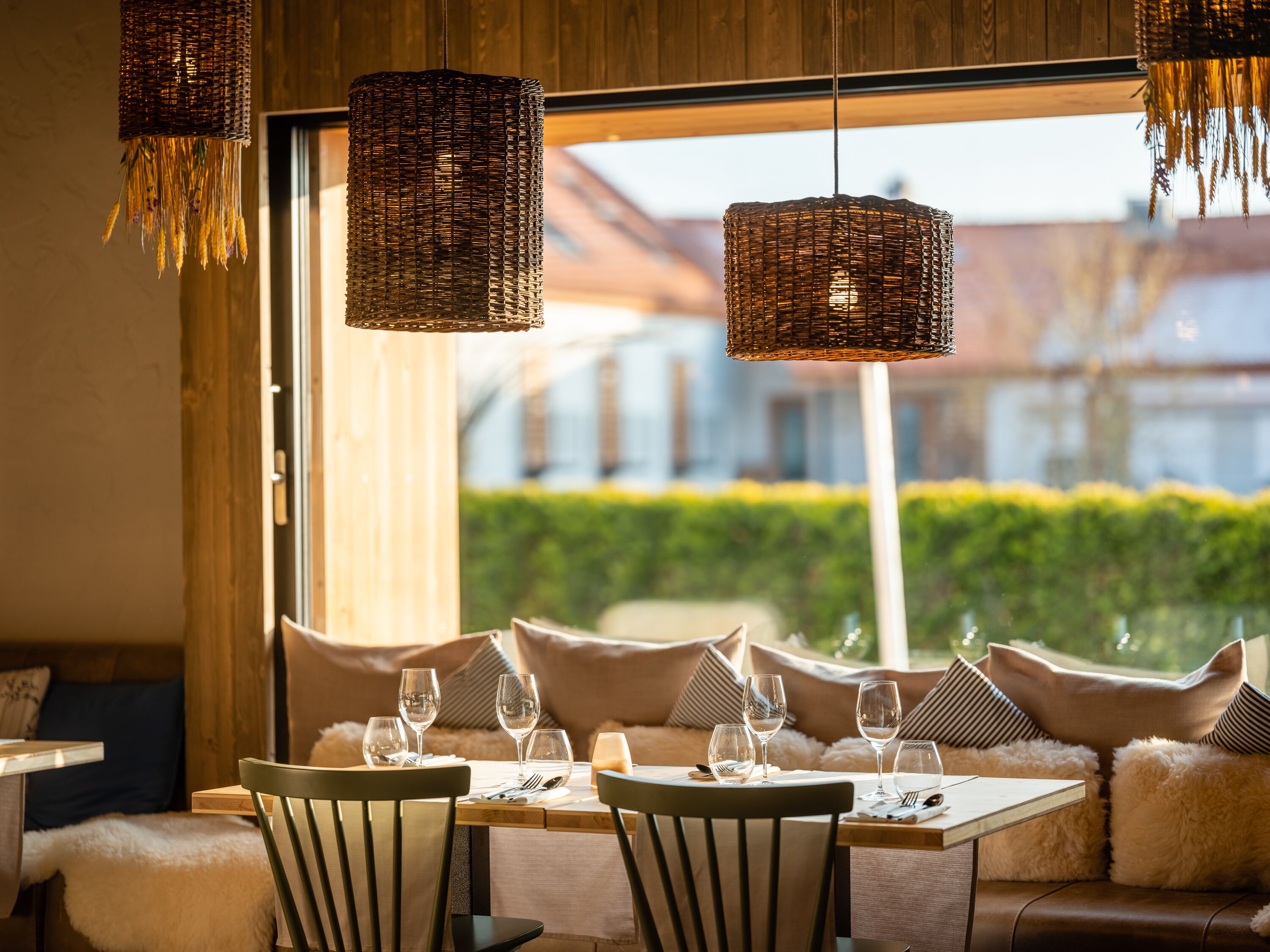 A dining area with wicker pendant lights, a table set for four, and a view of a residential area through large windows.