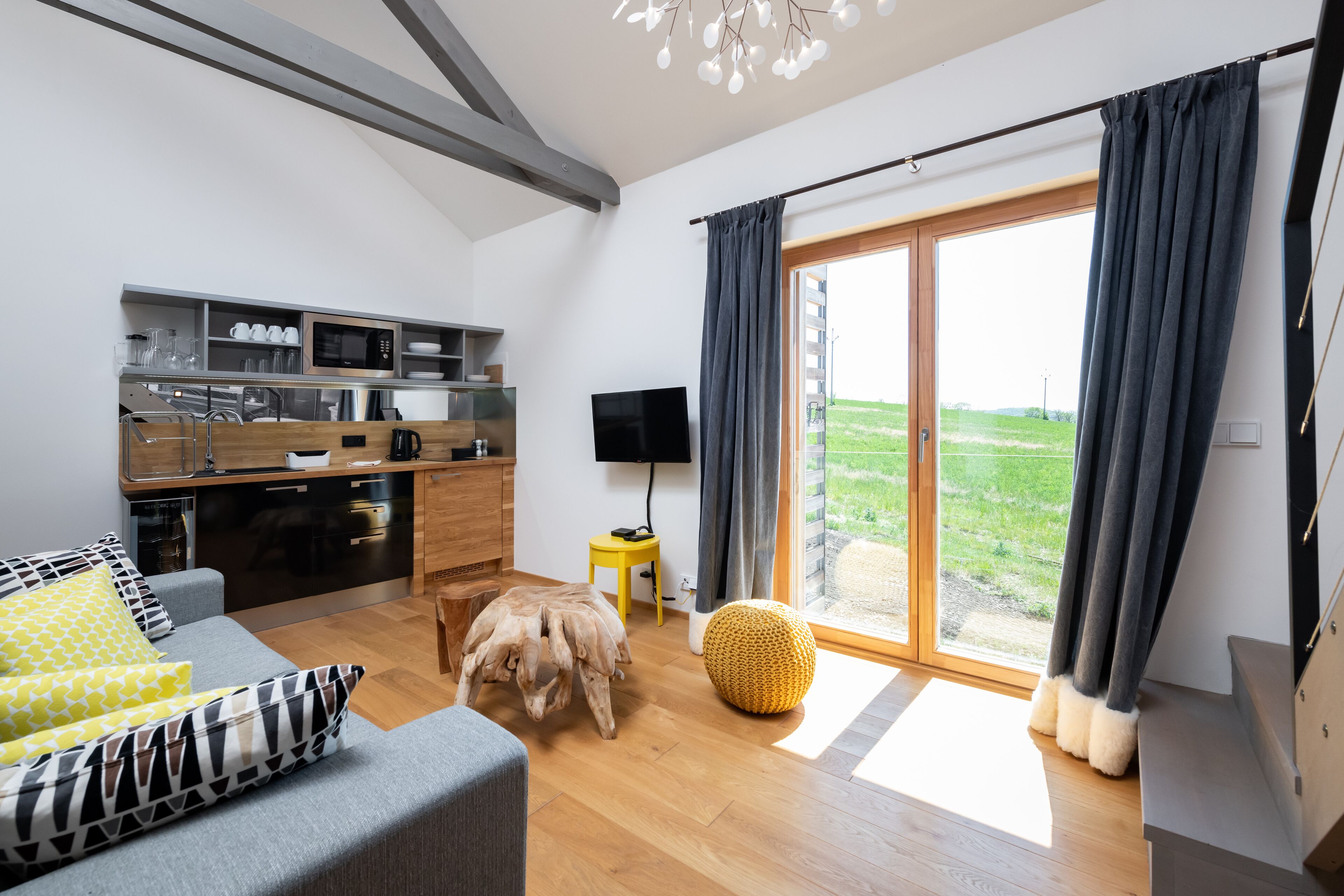 A modern living room with a grey sofa, wooden coffee table, and a large window with curtains.