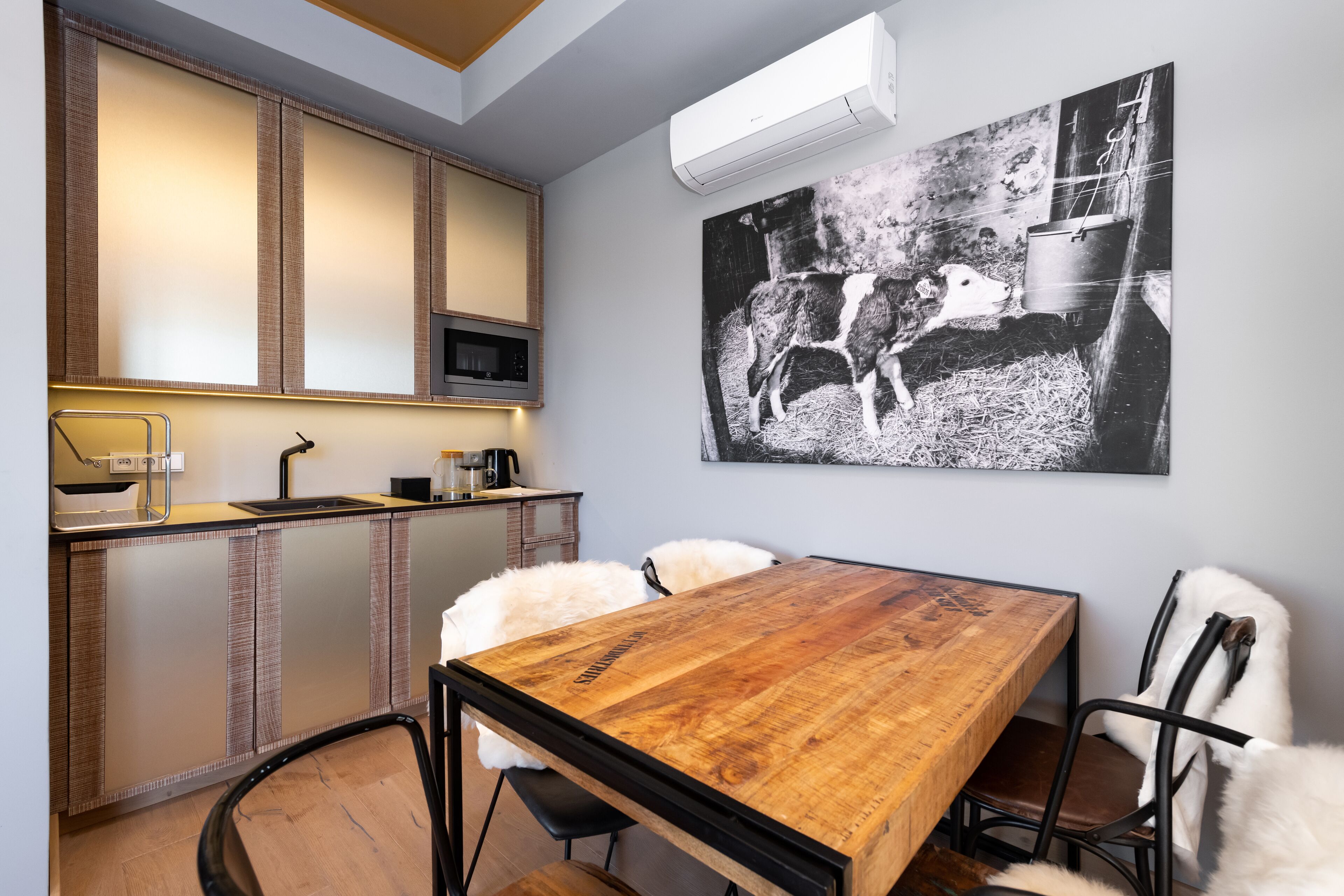 A modern kitchen with a wooden dining table, white fluffy chairs, and a black and white cow painting on the wall.