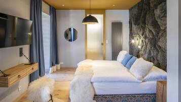 A modern bedroom with a large bed, a TV, a mirror, and a unique stone wall.