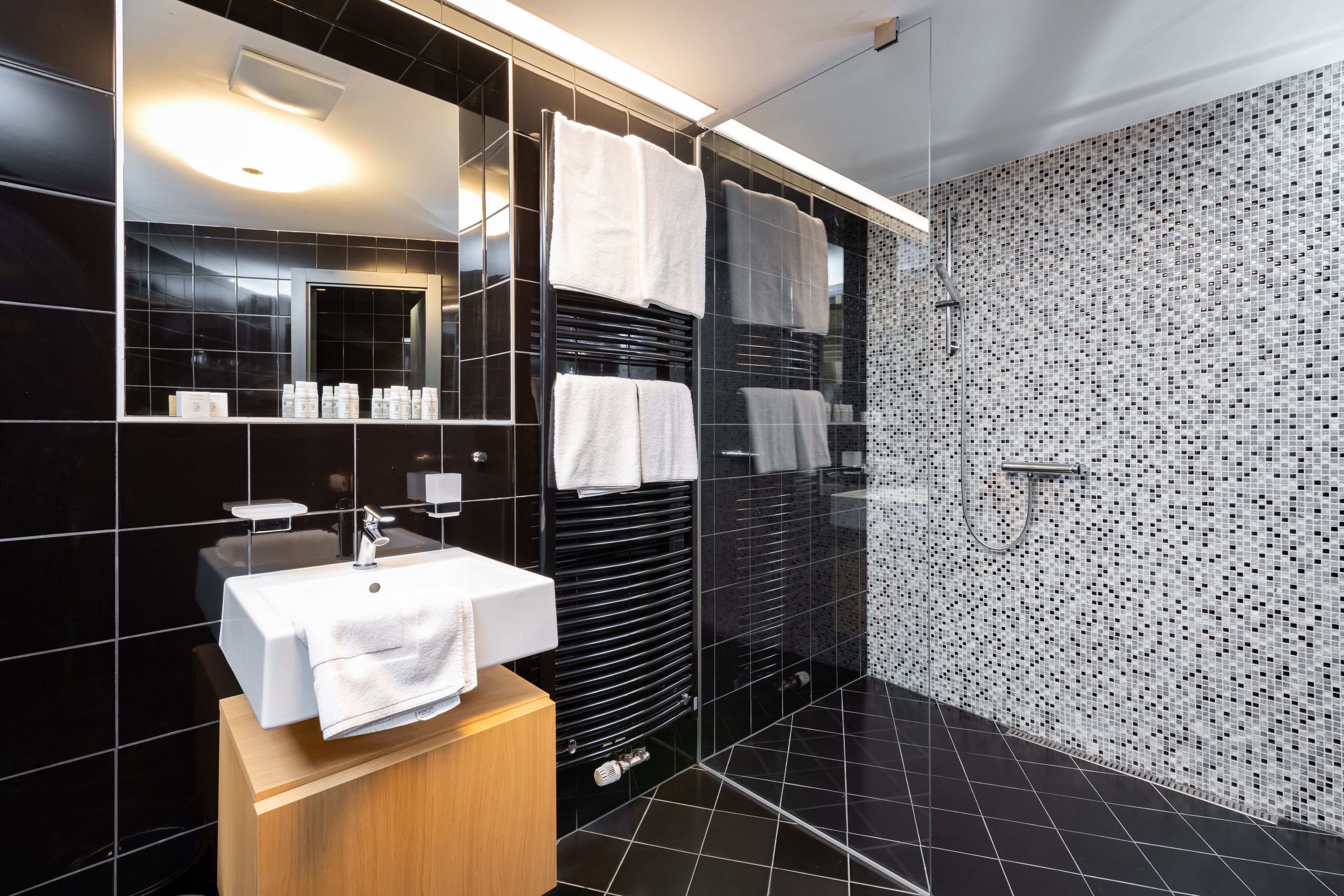 A modern bathroom with a black tiled wall, a white sink, and a mirror.