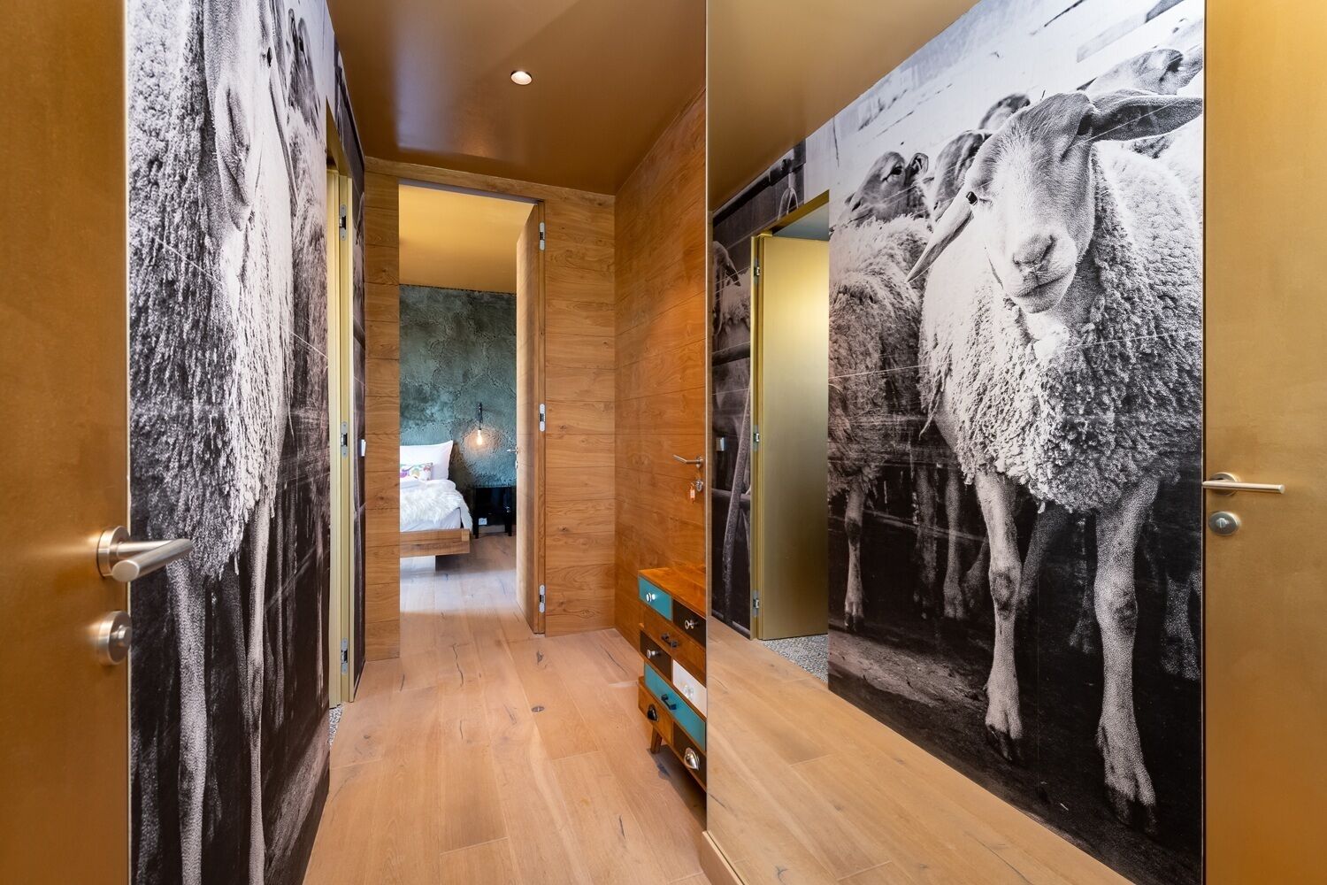 Un couloir aux murs en bois, orné d’une grande fresque représentant des moutons en noir et blanc sur l’un des murs.