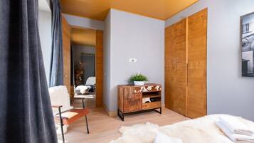 A modern bedroom with a wooden wardrobe, a small wooden dresser, a fluffy white rug, and a bed with white bedding.