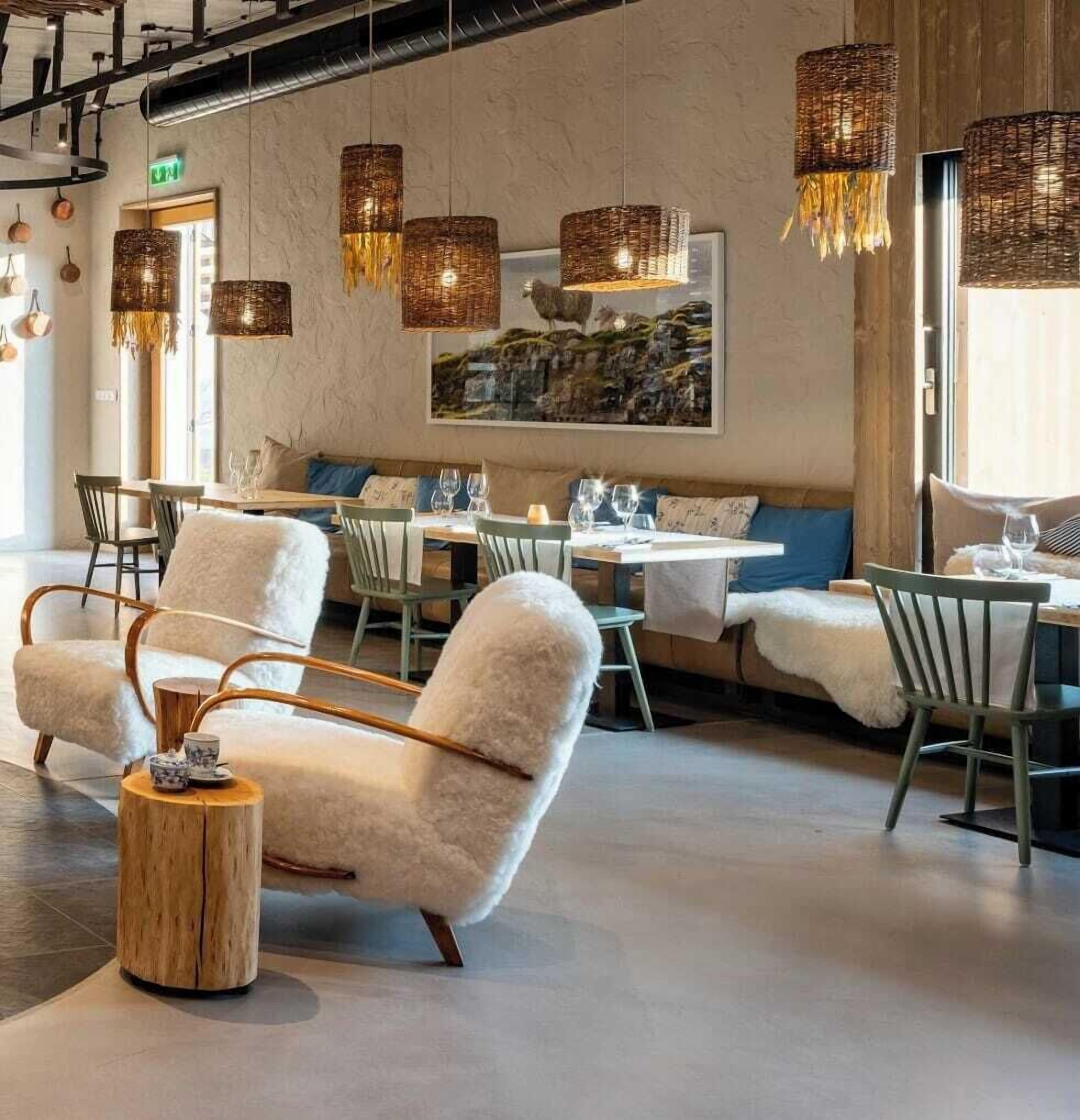 Un interior de restaurante moderno con lámparas colgantes de mimbre, asientos acolchados y una pared de piedra con un cuadro.